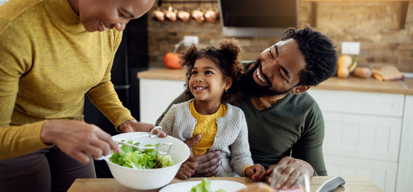 A young family sitting at a kitchen table with salad