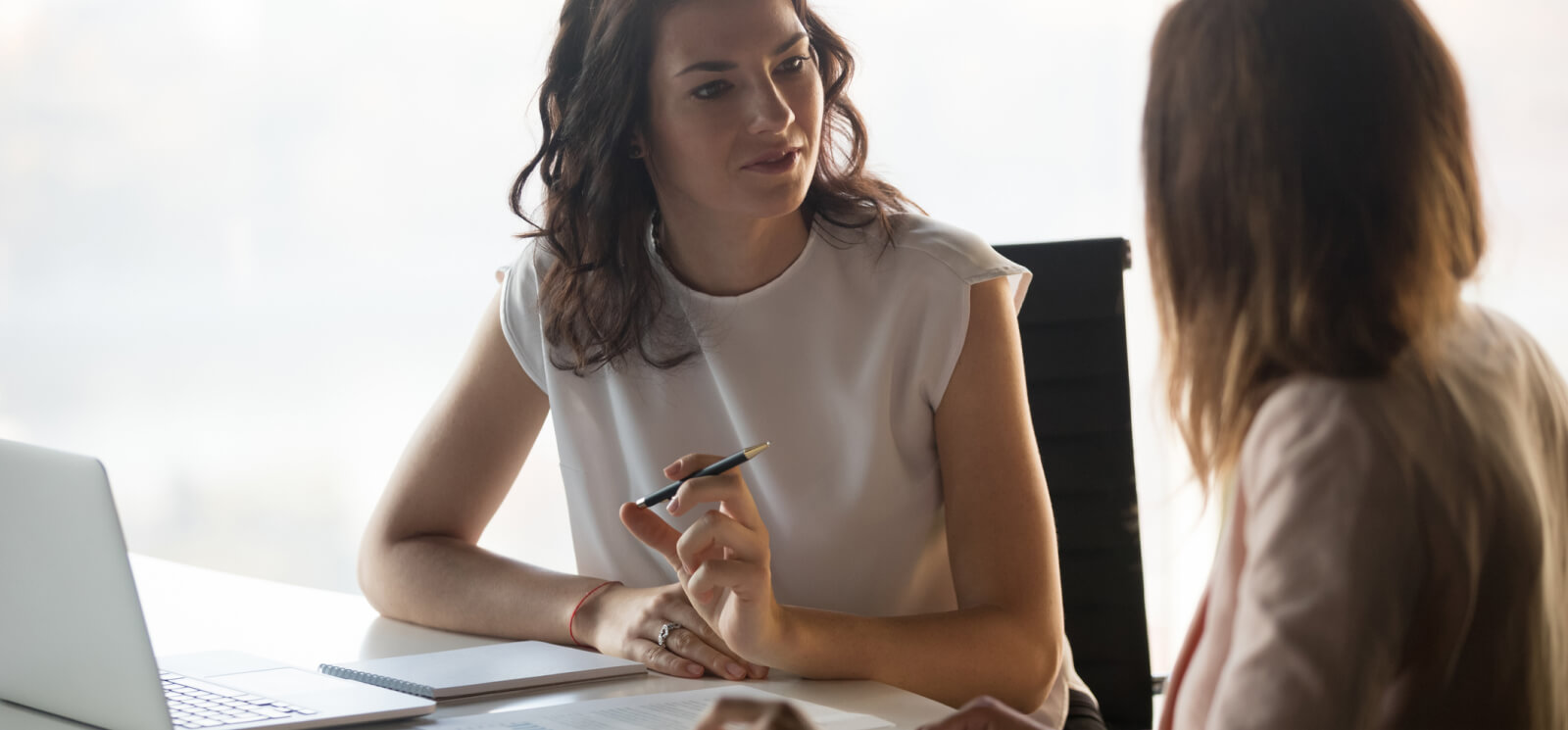 Two business women talking with a laptop on the table in front of them