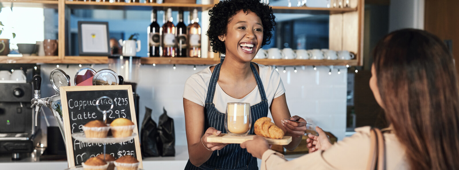 A woman working in a cafe handing a customer a tray with food and coffee