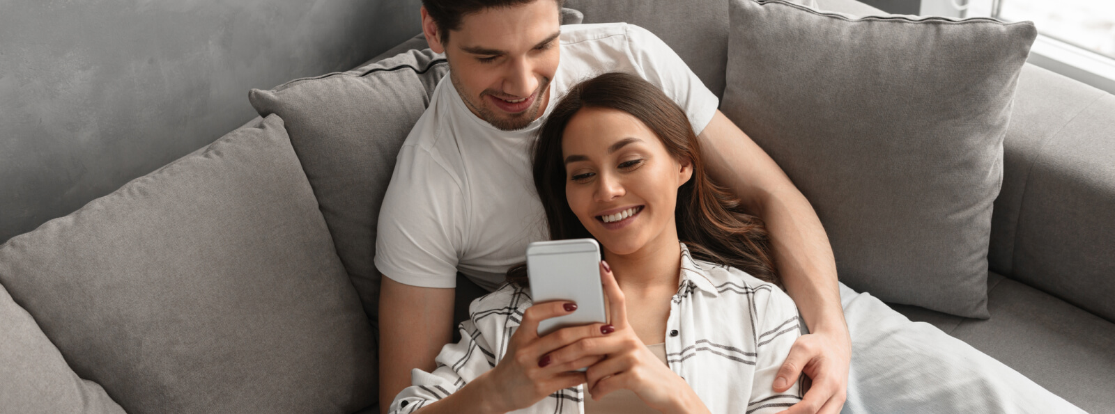 A young couple laying on a couch together looking at a smartphone